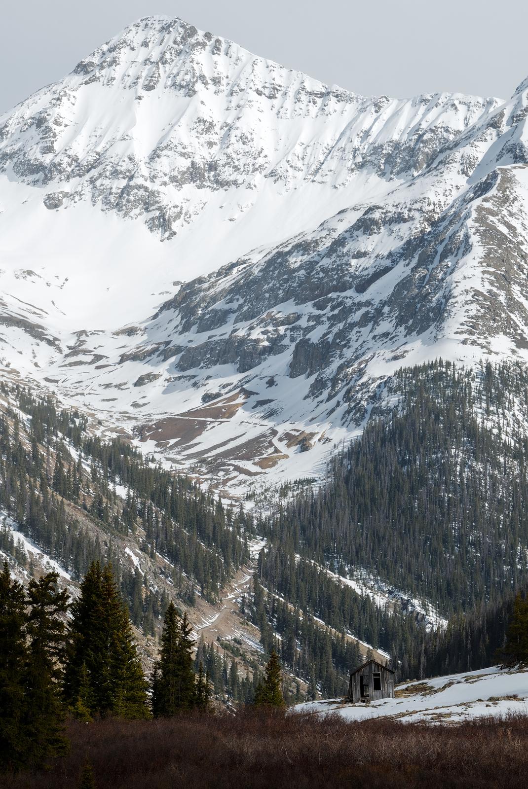 A lone cabin sits empty at Animas Forks, CO, with a large mountain in the background.