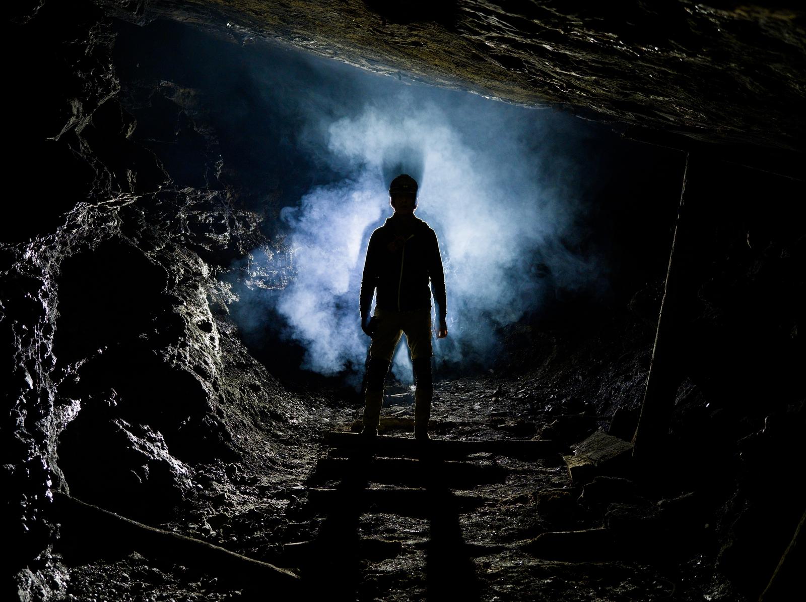 Deep in the mine on a photography expedition, an explorer's silhouette is seen in a cloud of cigarette smoke.