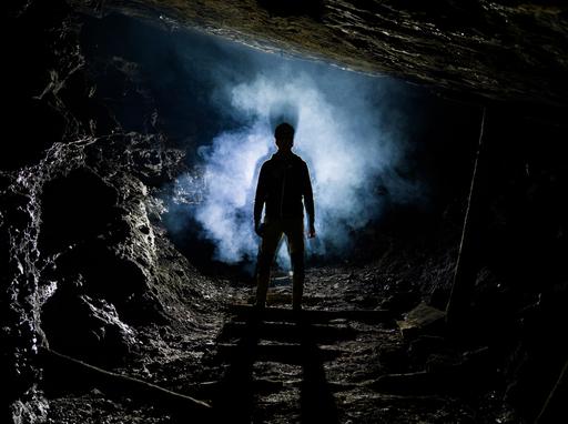Deep in the mine on a photography expedition, an explorer's silhouette is seen in a cloud of cigarette smoke.