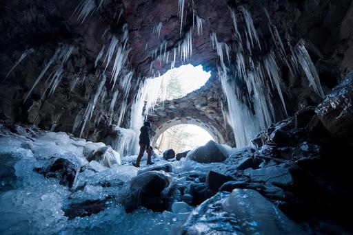 An explorer looks up into the light while surrounded by ice. This cave is actually a train tunnel that has been abandoned for at least 100 years. The far north portal protrudes from the mountain and has collapsed.